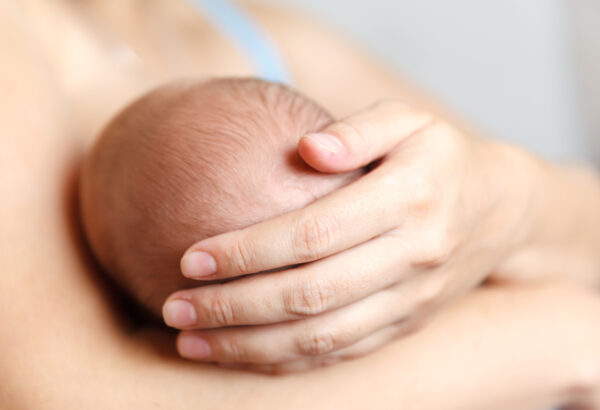 A mother holding a newborn baby close to her chest with her hand on the back of the baby's head.