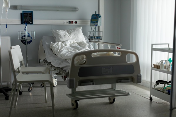 Empty hospital bed in a dimly lit room with medical equipment nearby, representing serious injury, critical illness, or a wrongful death in a healthcare setting.