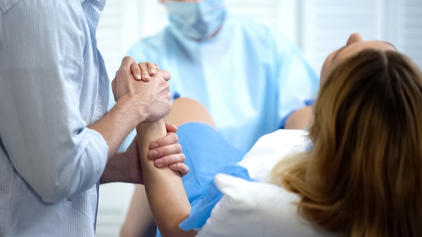 Woman in a hospital bed during childbirth holding her partner’s hand while a doctor in scrubs assists, representing labor and delivery or potential birth injury situations.