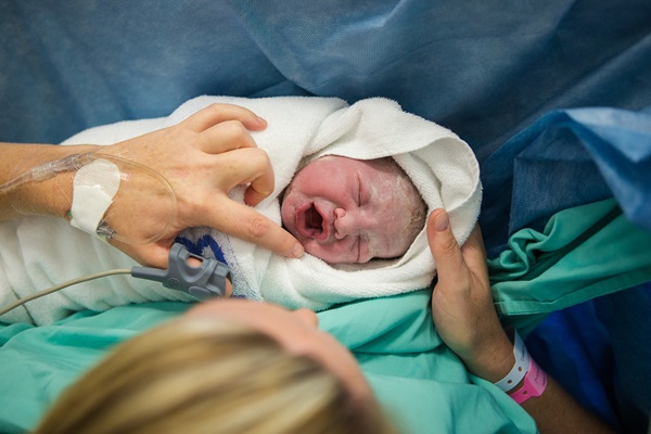 A newborn baby wrapped in a white towel being held by its mother shortly after being born.