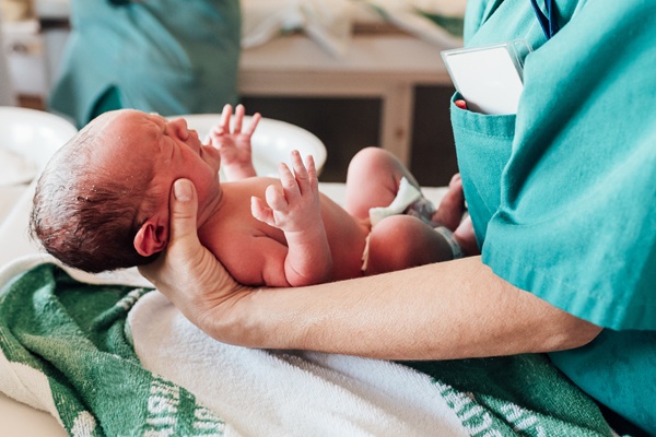 A healthcare professional in green scrubs holding a crying newborn baby on a medical table, representing an infant at risk for brain damage due to complications during birth.